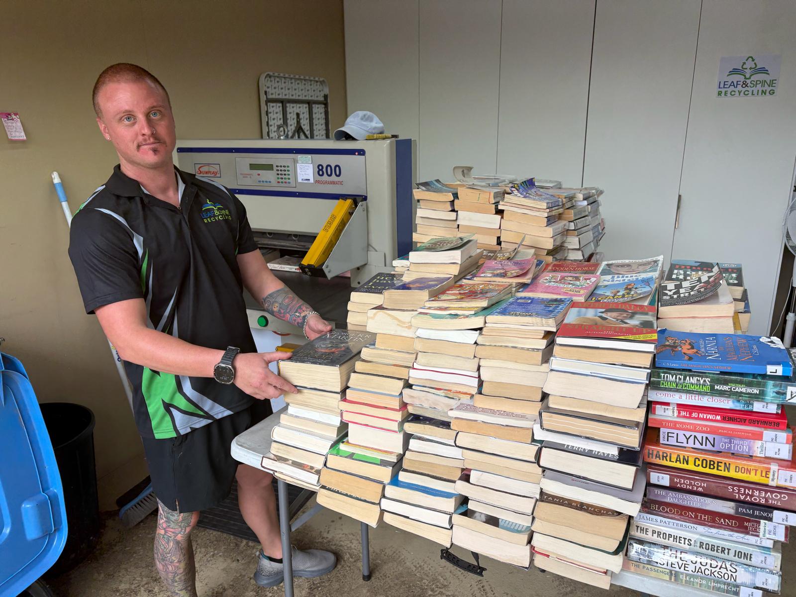 Leaf and Spine Recycling team member sorting weeded library books beside the guillotine used to remove book spines